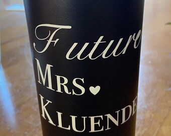 May include: Black insulated tumbler with a black lid. The tumbler has white cursive text that reads "Future Mrs. KLUENDE" with a heart symbol. The tumbler is on a wooden surface.