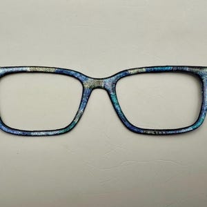 May include: A pair of blue, green, and gold patterned eyeglasses with a rectangular frame.