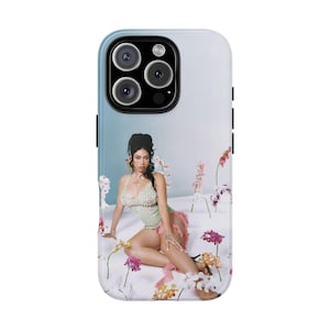 May include: A phone case featuring a woman in a light green and pink outfit surrounded by flowers. The case has a blue and white gradient background and a black camera module.