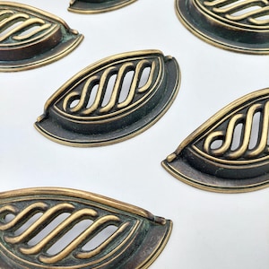 May include: A collection of six semi-circular metal drawer pulls featuring an antique brass finish with a dark patina. Each pull has a decorative openwork design consisting of four diagonal, curved bars enclosed within a solid metal frame.