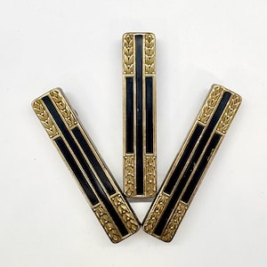 May include: Three rectangular hair clips arranged in a fan shape. Each clip features a central black vertical stripe flanked by gold-toned metal borders with an embossed leaf pattern at the top and bottom ends of the rectangular frame.