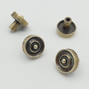 May include: Four antique brass cabinet knobs. Each knob has a circular face with concentric rings and a central stud. The knobs are a warm, aged brass color, suggesting vintage or rustic decor. The knobs are designed for furniture.