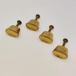 May include: Four vintage brass cabinet knobs with a screw post. The knobs have a rounded, conical shape and a tarnished, aged appearance. The brass has a warm, golden hue, and the screws are a darker, contrasting color. The knobs are arranged on a white surface.