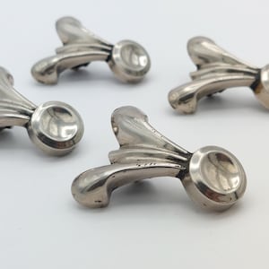 May include: Close-up of four silver-toned decorative hardware pieces. Each piece has a curved, ornate design with a circular end. The hardware is likely for furniture or cabinetry, adding a touch of elegance.