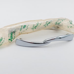 May include: A shiny chrome-plated door handle with a curved design. The handle is packaged in a clear plastic wrapper with green text that reads "Genuine Ameroc Made in U.S.A."