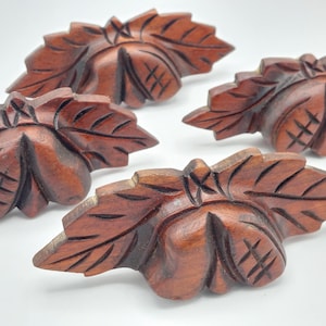 May include: Four intricately carved wooden leaf-shaped decorative accents. Each piece is a rich, dark brown color with detailed veining and a central nut-like form. The carvings are likely for furniture or craft projects.