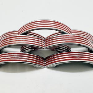 May include: A set of five arched drawer pulls featuring a metallic silver finish with recessed horizontal red stripes. Each handle has a curved, semi-circular shape with a smooth, polished surface and distinct grooves running along the length.