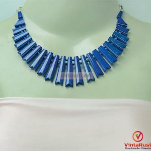 May include: A striking blue necklace with a geometric design. The necklace features rectangular, angled pieces in a deep blue hue, connected by small silver beads. The necklace is displayed on a mannequin.