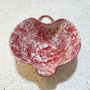 May include: A red and white speckled ceramic bowl with a handle. The bowl is heart-shaped and has a speckled glaze.