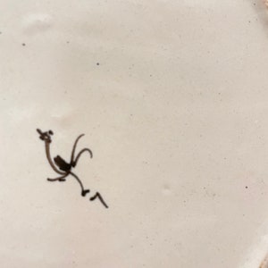 May include: White ceramic plate with a blue and white design. The underside of the plate features a hand-drawn black rooster.