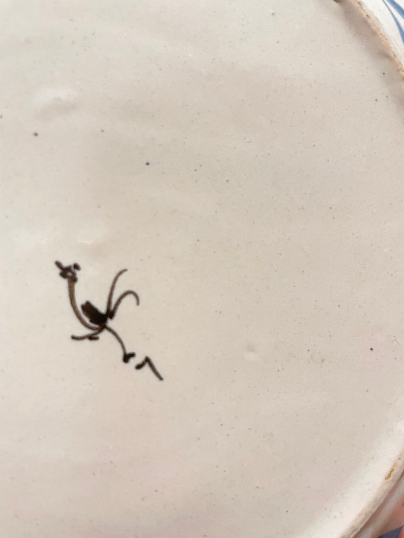 May include: White ceramic plate with a blue and white design. The underside of the plate features a hand-drawn black rooster.