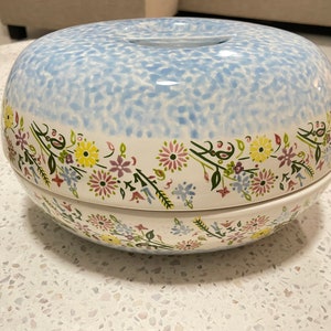 May include: A two-piece ceramic serving dish with a blue and white speckled glaze. The top piece has a hole in the center and both pieces are decorated with a floral border in shades of pink, yellow, and blue.