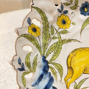 May include: A white ceramic plate with a blue and yellow floral design and a yellow deer. The plate has a scalloped edge and a cut-out design.