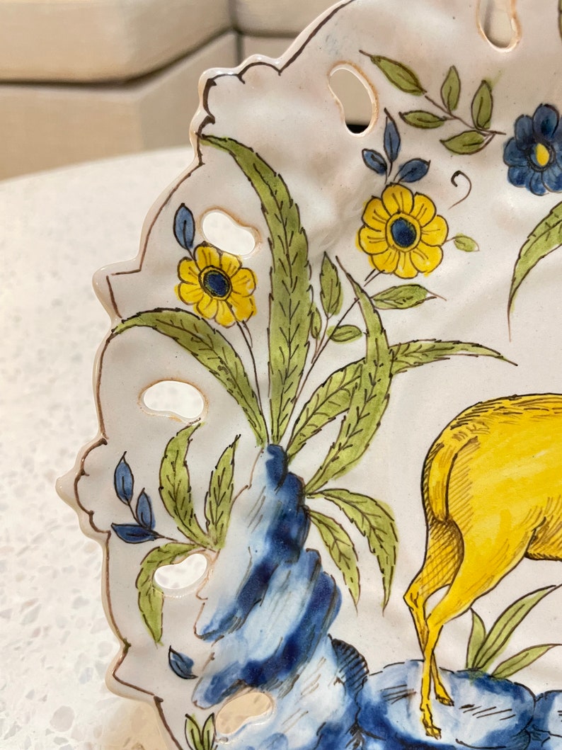 May include: A white ceramic plate with a blue and yellow floral design and a yellow deer. The plate has a scalloped edge and a cut-out design.