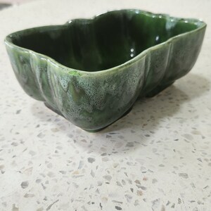 May include: A green ceramic planter with a wavy, irregular rim. The planter has a mottled green glaze with a slightly lighter green color in the center.