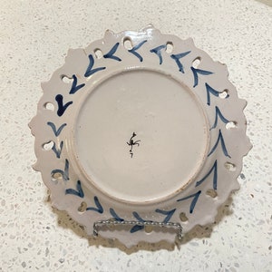 May include: White ceramic plate with a blue and white design of arrows around the edge. The plate has a scalloped edge and is decorated with a blue and white floral design. The back of the plate has a small black mark.