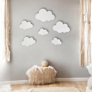 May include: A white wall with a fluffy rug and a small, fluffy stool. The wall is decorated with seven white paper clouds of various sizes.