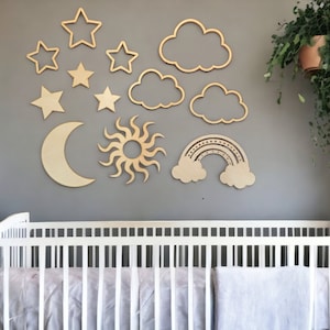 May include: A white crib with a wooden sun, moon, stars, clouds, and rainbow cutout decorations on the wall behind it. A potted plant hangs from the ceiling.
