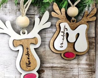 May include: Two wooden reindeer ornaments with names "Theodore" and "Madalyn" written on them. The ornaments are white with brown accents and have red noses.