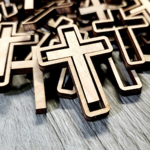 May include: A pile of wooden crosses with a natural wood finish. The crosses are stacked on top of each other, creating a layered effect. The crosses are all the same size and shape, and they have a simple, elegant design.