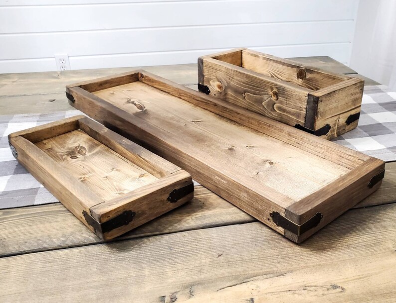 May include: Three wooden trays with metal accents. The trays are of different sizes and are stacked on top of each other. The trays are made from natural wood and have a rustic look.