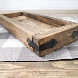 May include: A rustic wooden tray with a rectangular shape and a natural wood finish. The tray has metal corner accents and is sitting on a checkered fabric.