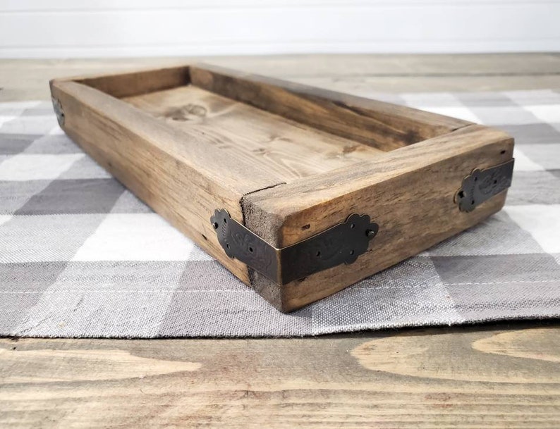 May include: A rustic wooden tray with a rectangular shape and a natural wood finish. The tray has metal corner accents and is sitting on a checkered fabric.