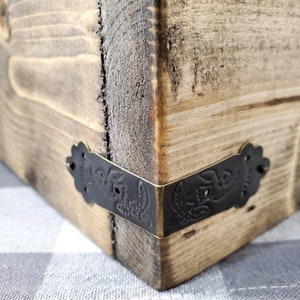 May include: Close-up of a wooden box corner with black metal corner brackets. The brackets have a decorative floral design.