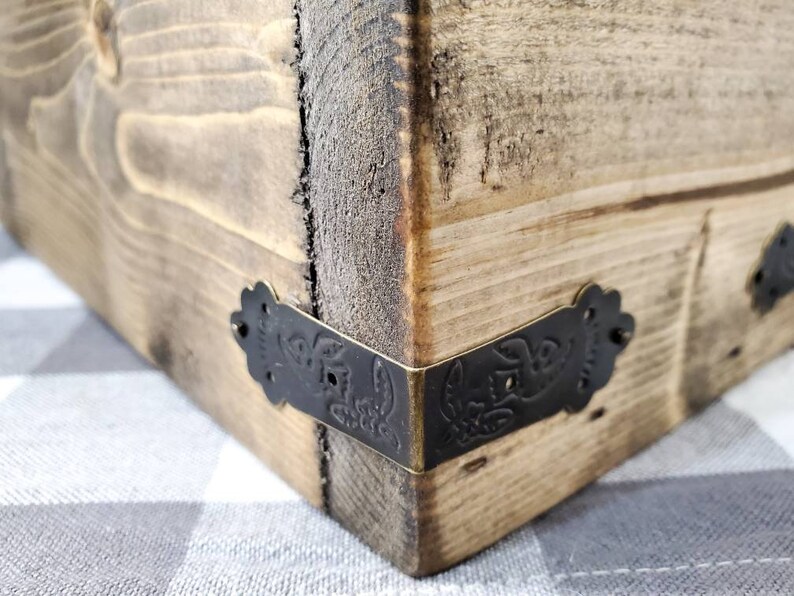 May include: Close-up of a wooden box corner with black metal corner brackets. The brackets have a decorative floral design.