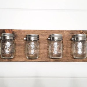 May include: A wooden wall-mounted shelf with four glass jars with metal lids. The jars are empty and the shelf is stained a dark brown color.
