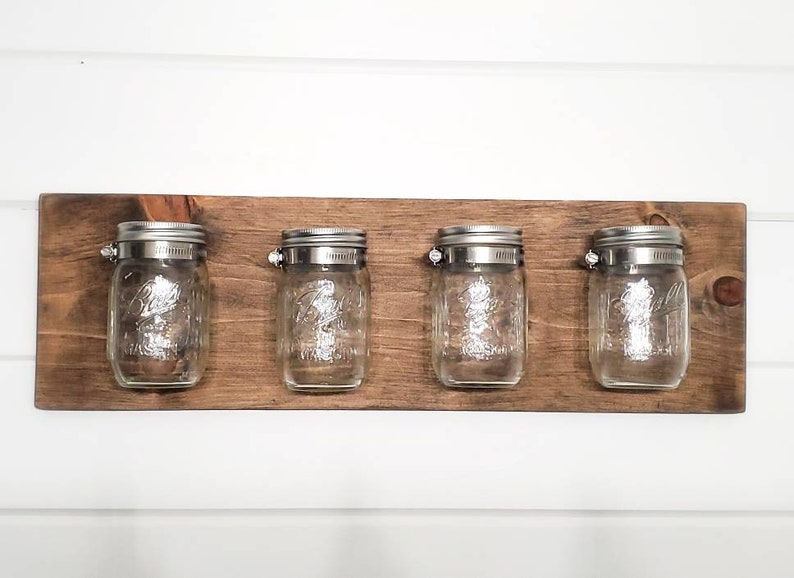 May include: A wooden wall-mounted shelf with four glass jars with metal lids. The jars are empty and the shelf is stained a dark brown color.