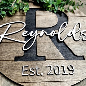 May include: A wooden sign with the last name "Reynolds" and the year "Est. 2019" in white lettering. The letter "R" is a large black cutout.