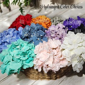May include: A collection of artificial hydrangea flower heads in a woven basket, labeled Hydrangea Color Choices. Colors include red, fall orange, gray, dark purple, black, white, pink, teal, dusty blue, and light blue, each with text labels.