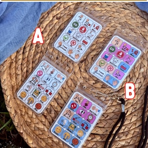 May include: Four communication boards with various icons and text, including "Two Options Available." The boards are in clear plastic sleeves, with a black lanyard attached to one. The boards feature words like "Drink," "Yes," and "Happy."