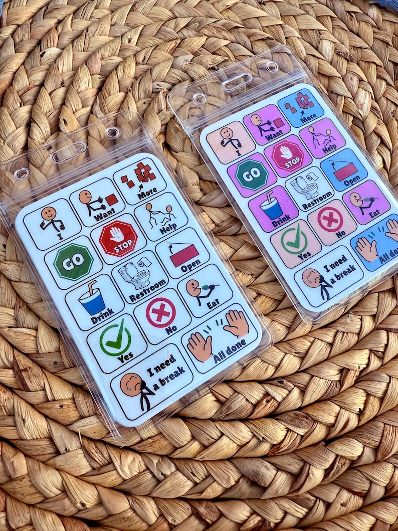 May include: Two communication boards with clear plastic sleeves, featuring colorful icons and text. The boards include symbols for "Go," "Stop," "Drink," "Restroom," and "Eat." The text includes "Want," "More," "Help," "Yes," "No," "I need a break," and "All done."