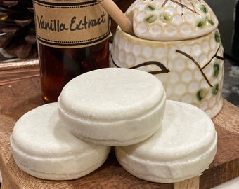 May include: Three white round shampoo bars stacked on a wooden cutting board. The bars are made of natural ingredients and are free of sulfates, parabens, and silicones. The bars are a sustainable alternative to traditional shampoo.