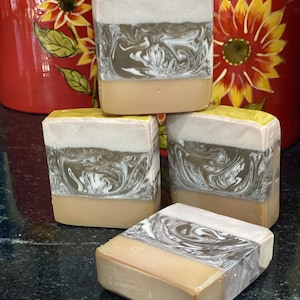May include: Four bars of handmade soap with a brown and white swirl design. The soap bars are stacked on top of each other. The soap bars have a light brown base and a white top layer with brown swirls.