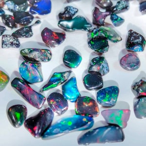 Può includere: Una collezione di pietre preziose di opale nero iridescente, ognuna con un motivo unico di colore e luce.