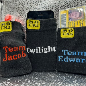 May include: Three black socks with yellow and red logos. The socks have the text "Team Jacob" and "Team Edward" printed on them. The socks are for holding a phone or ID card.