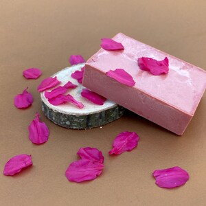 May include: Two pink soap bars on a wooden slice with pink flower petals scattered around.