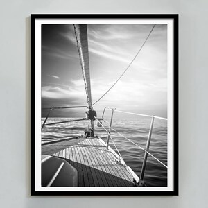 Puede incluir: Fotografía en blanco y negro de un velero en el agua. La foto está tomada desde la cubierta del barco, mirando hacia adelante. El mástil y el aparejo son visibles, así como las olas.