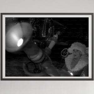May include: Black and white photograph of a woman in a Santa hat and fur-trimmed coat, holding a decorative object. The image is framed and features a blurred background with lights, suggesting a festive or performance setting.