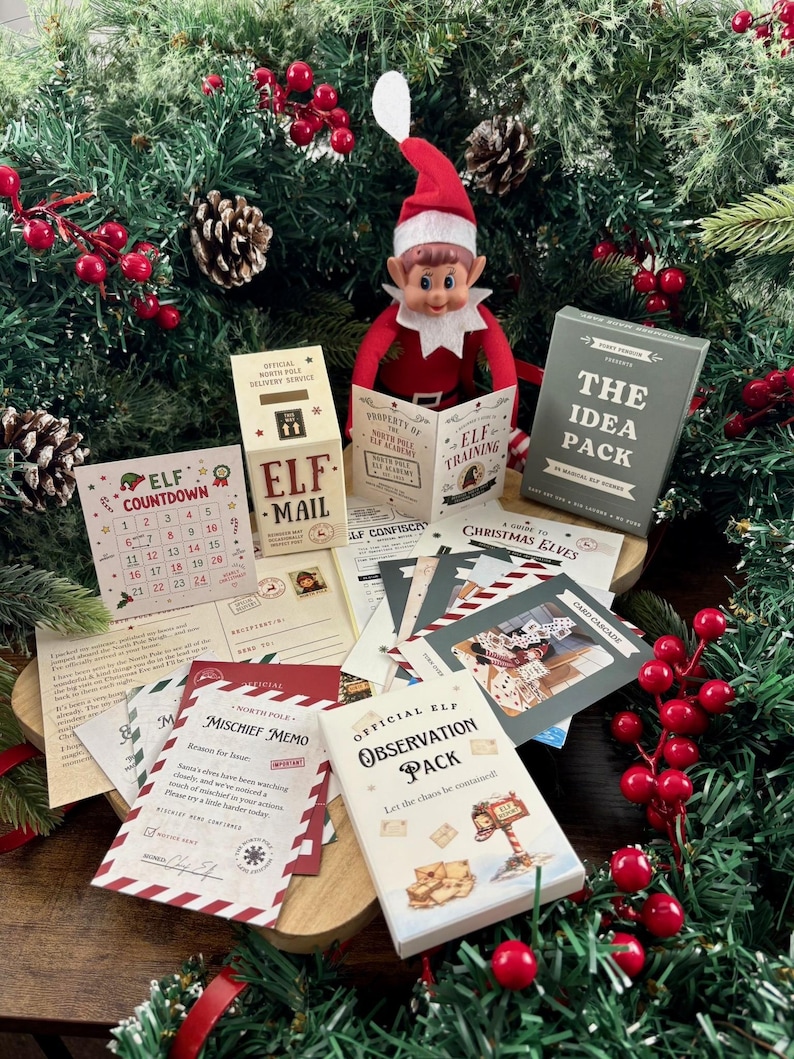 Pu&ograve; includere: Una bambola elfo di Natale con cappello e tuta rossa siede dietro una collezione di articoli di carta stampata, tra cui una scatola Elf Mail, un calendario Elf Countdown, un Mischief Memo, un Observation Pack e The Idea Pack con varie carte.