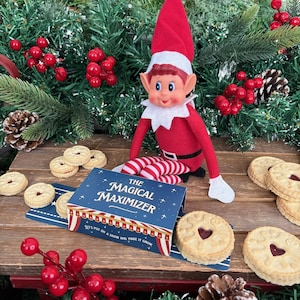 May include: A festive scene featuring a red and white elf doll, biscuits, and Christmas greenery. A blue box with the words "The Magical Maximizer" is open, and the elf is surrounded by treats.