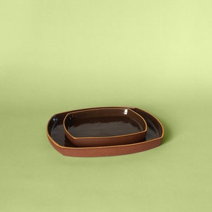May include: Two rectangular ceramic trays, one nested inside the other. The larger tray is brown with a light brown rim. The smaller tray is dark brown with a light brown rim.