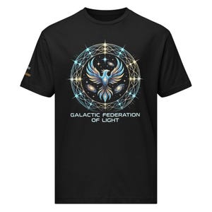 Puede incluir: Camiseta negra con un diseño detallado de un fénix con detalles en azul y dorado, rodeado por un diseño celestial. El texto "GALACTIC FEDERATION OF LIGHT" está impreso debajo. La camiseta es de material suave.