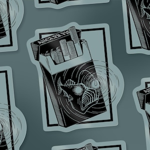 Op de afbeelding: Zwart-witte sticker met een sigarettenpakje ontwerp met de tekst "ANGLER FISH". Het pakje is open en onthult sigaretten. Het ontwerp bevat een illustratie van een zeeduivel en concentrische cirkels.