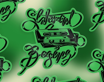 May include: Green sticker featuring the text "Statement Designs" in a decorative font, and a black and white cassette tape illustration. The sticker has a glossy finish and a rounded edge.