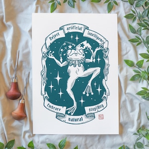 Op de afbeelding: Een grillige kunstprint met een kikker in een narrenkap, omringd door sterren en de woorden "Reject Artificial Intelligence, Embrace Natural Stupidity". De illustratie is in teal en wit, met een rode stempel in de hoek.