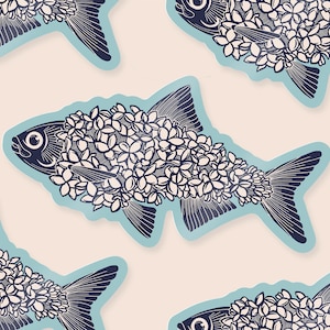 Op de afbeelding: Een herhalend patroon van gestileerde visillustraties. Elke vis is omlijnd in een lichtblauwe kleur en gevuld met witte bloemmotieven. De vissen hebben donkerblauwe vinnen en ogen, tegen een lichtroze achtergrond.